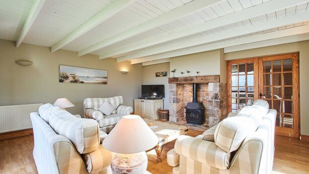 A cozy living room with a fireplace, sofas, a TV, and a stone wall. - Host & Stay | The Coach House (Beal)