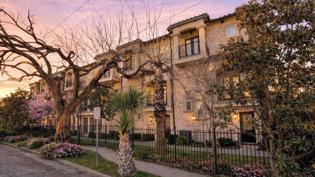 Un edificio de varios pisos con fachada de piedra, un patio central y un árbol con ramas desnudas.