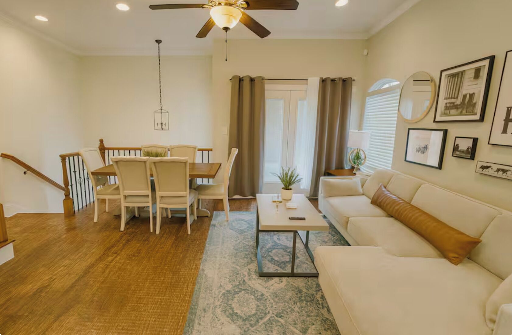 A living room with a sofa, a dining table with chairs, a ceiling fan, and a staircase.