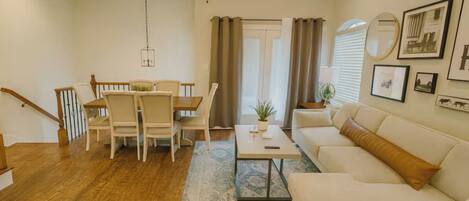 A living room with a sofa, a dining table with chairs, a ceiling fan, and a staircase.