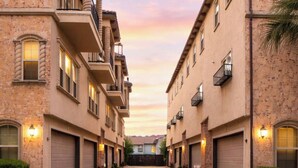 A row of multi-story residential buildings with balconies and garage doors, set against a sunset sky.