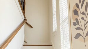 Una escalera con barandillas de madera, paredes blancas y un ventanal con persianas.