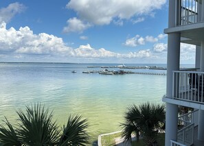 Une vue d’une marina avec des bateaux amarrés, un ciel dégagé et un bâtiment doté de balcons donnant sur l’eau.