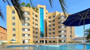 Ein mehrstöckiges Hotel mit Swimmingpool, Palmen und einem blauen Sonnenschirm.