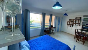 Ein Schlafzimmer mit einem Bett, einem Schreibtisch und einem Stuhl. Es gibt ein Fenster mit Vorhängen, eine Deckenleuchte und einen Fernseher an der Wand.