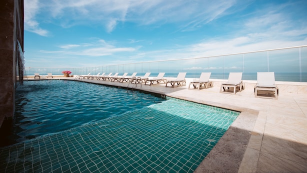 A rooftop infinity pool with a clear view of the ocean, surrounded by lounge chairs and a glass railing. - Palmetto Beach 1402 & Sea View - Hot Water- 2bth (Cartagena)