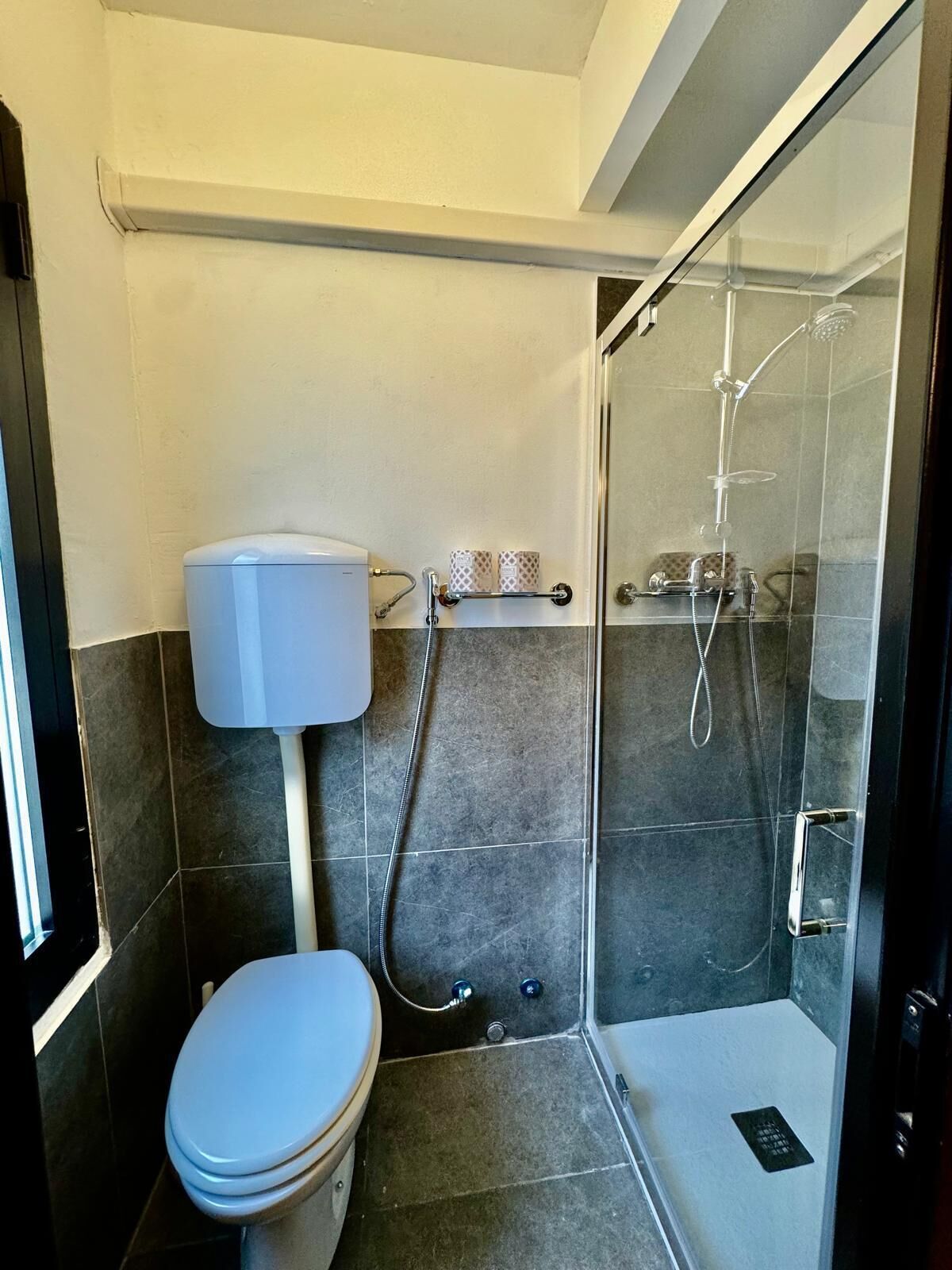 Un baño pequeño y moderno con inodoro, ducha y cabina de ducha de vidrio.