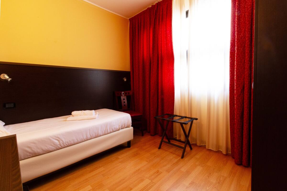 A hotel room with a bed, a wooden headboard, a desk, and a chair.