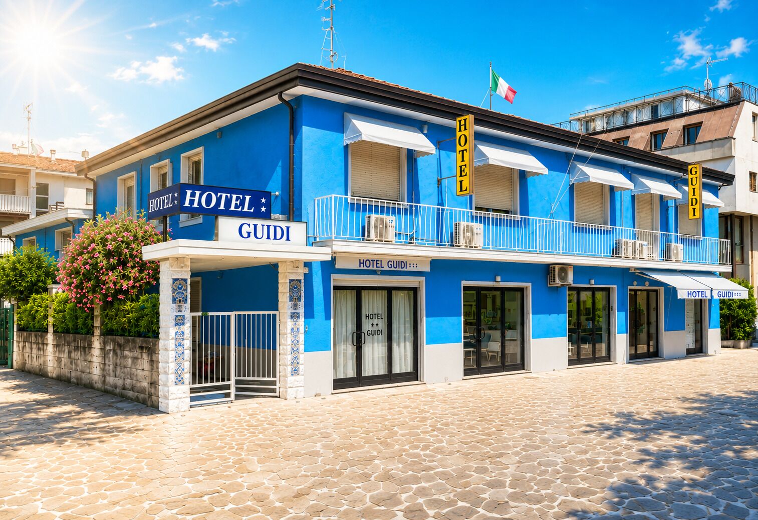A hotel with a blue facade, balconies, and a sign reading 'HOTEL GUIDI'.