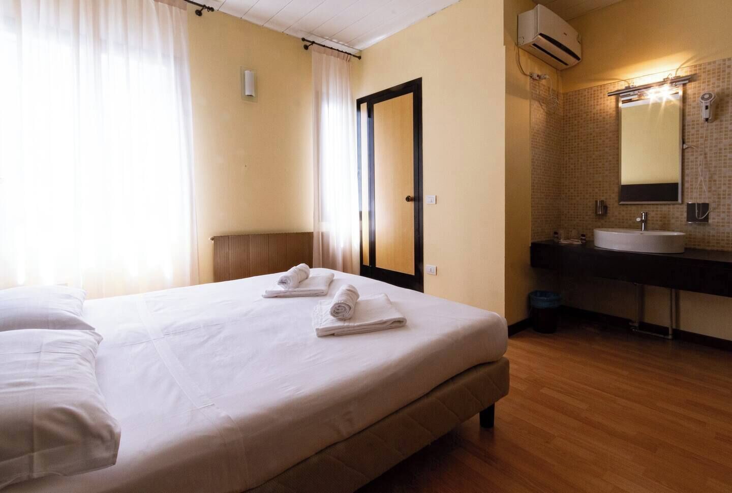 A hotel room with a bed, a bathroom with a sink and mirror, and a door.