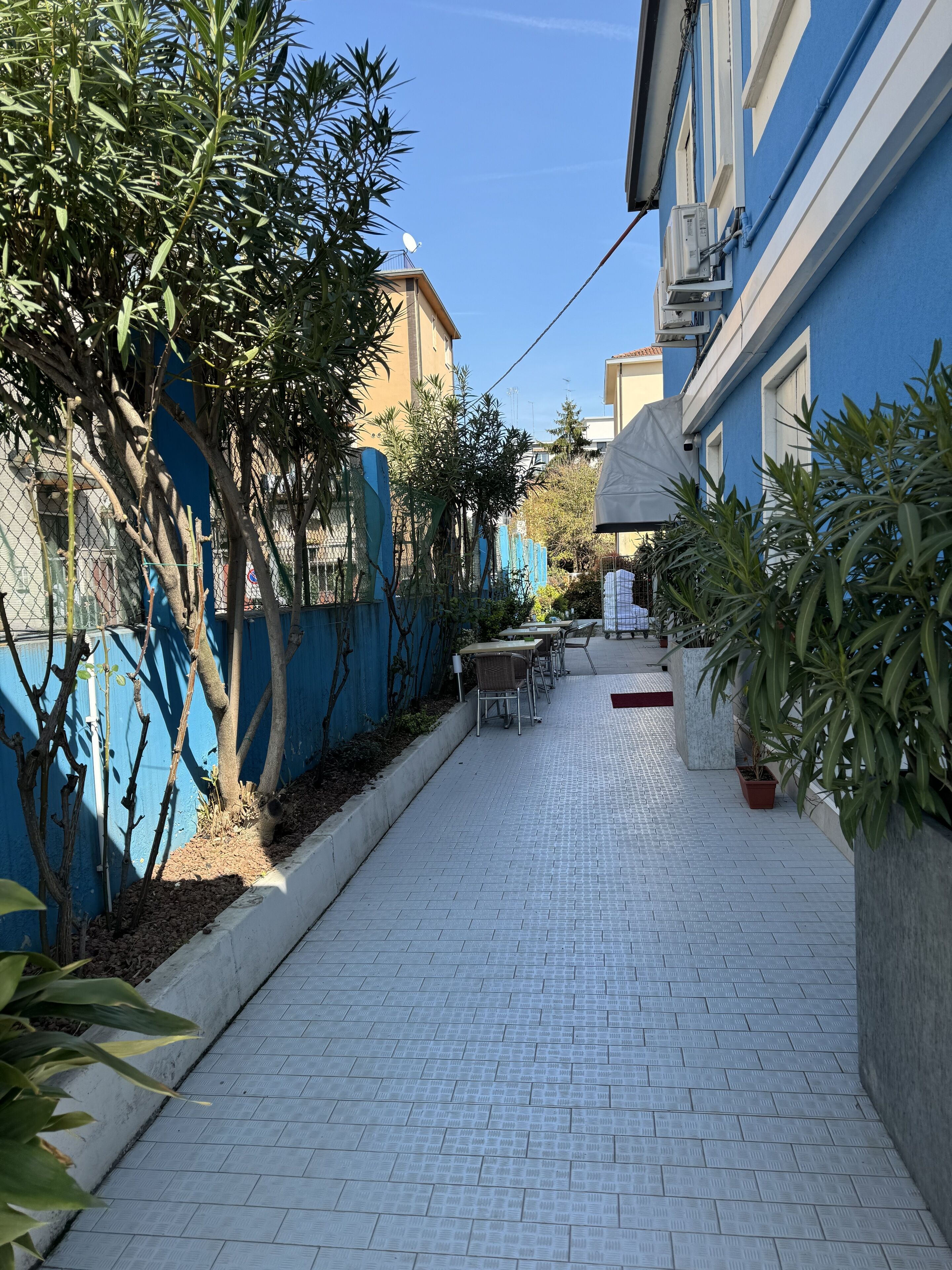A narrow paved courtyard with a tiled floor, surrounded by blue walls and trees.