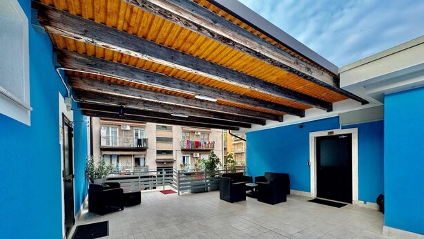 An outdoor patio area with tiled flooring, black outdoor furniture, and a wooden ceiling. - Hotel Guidi (Mestre)