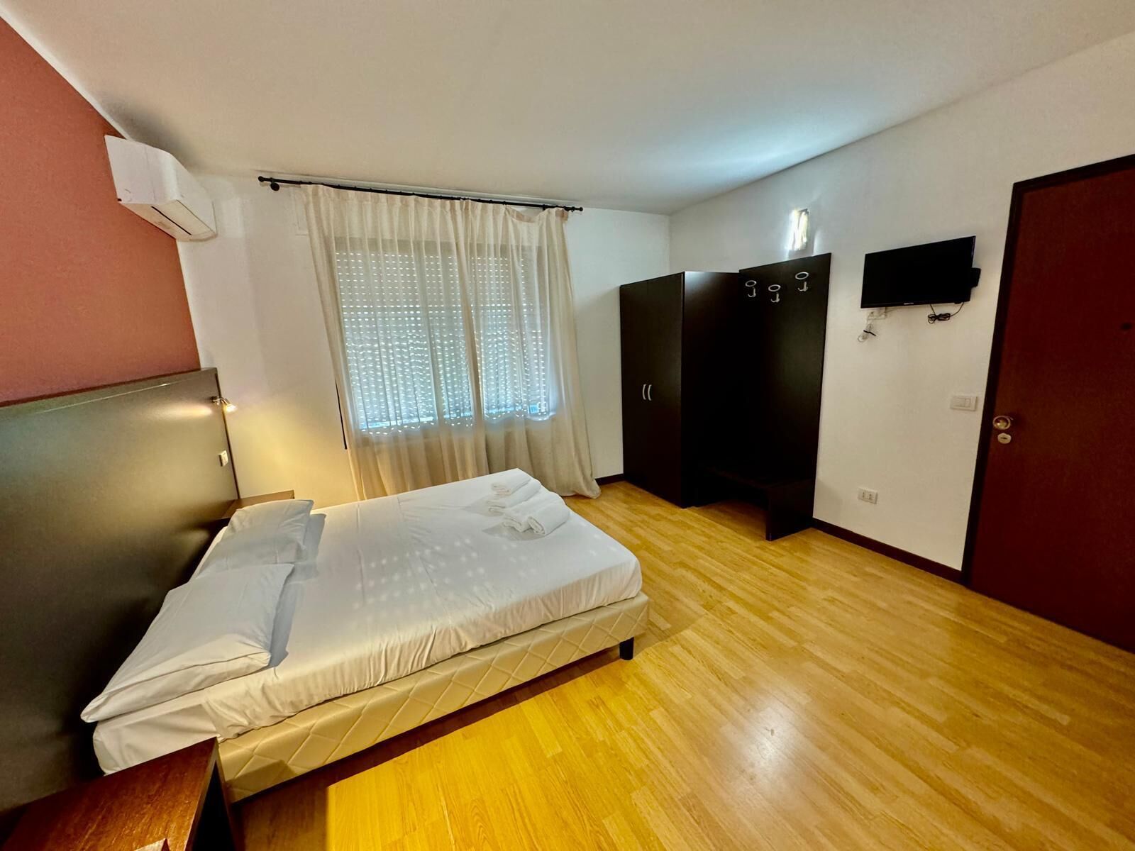 A hotel room with a bed, a wardrobe, a TV, and a window with curtains.