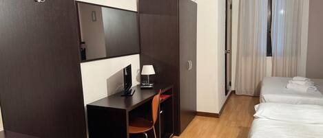 A hotel room with a desk, chair, two beds, and an air conditioning unit.