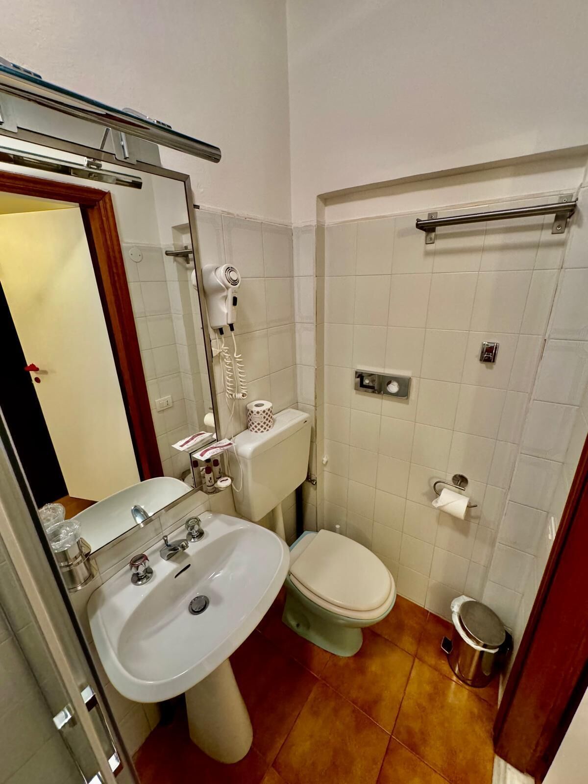 Une petite salle de bain avec un lavabo blanc, des toilettes et un sèche-cheveux fixé au mur.