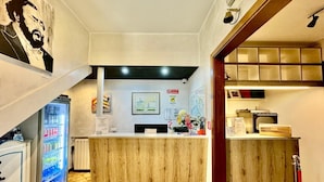A reception area with a wooden reception desk, a refrigerator stocked with beverages, and a security camera above the desk. - Hotel Guidi (Mestre)