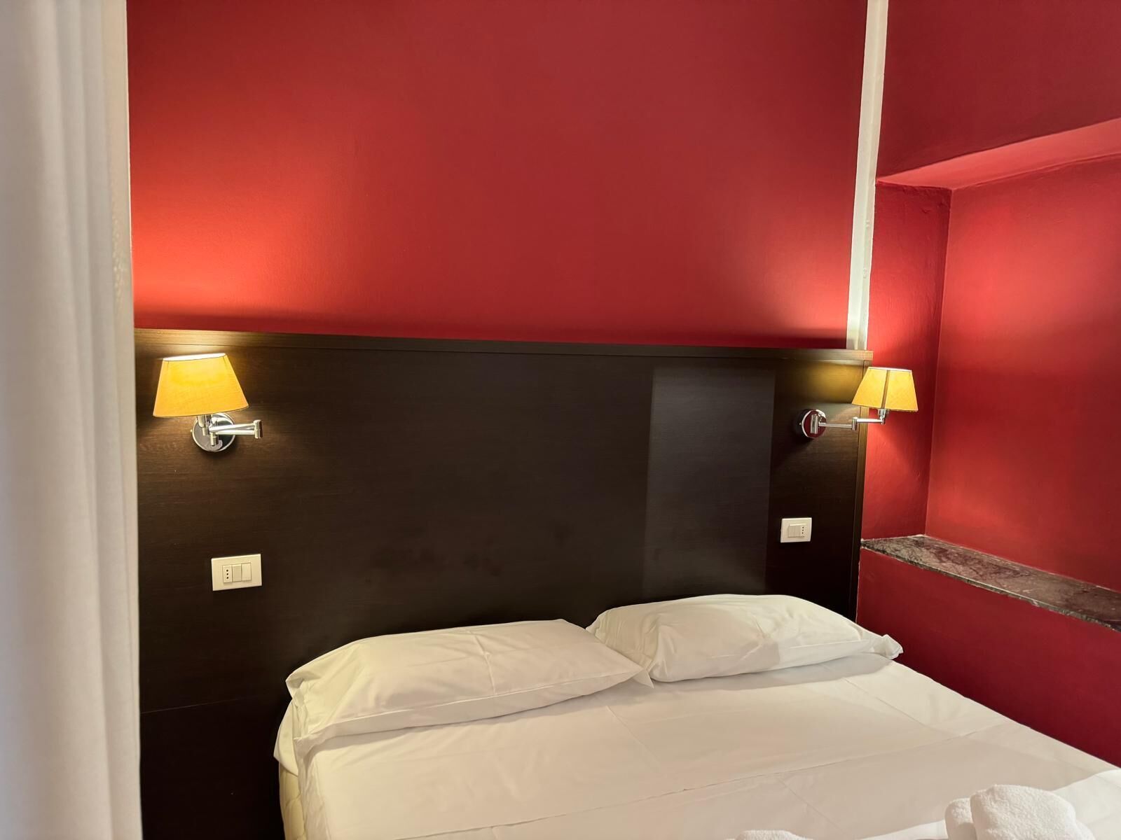 A hotel room with a red wall, a black headboard, and two bedside lamps.
