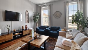 A modern living room with a flat-screen TV, a wooden coffee table, a sofa, and two blue armchairs.