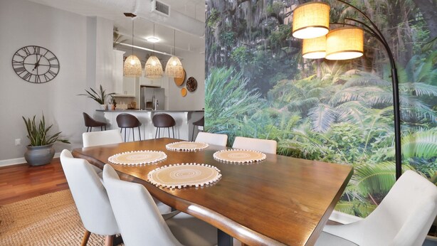A dining area with a wooden table, white chairs, and a large mural of a forest.