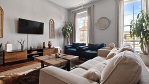A modern living room with a flat-screen TV, a wooden coffee table, a sofa, and a large window with curtains.