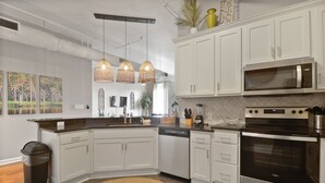 A modern kitchen with white cabinets, a stainless steel oven, a microwave, and pendant lights.