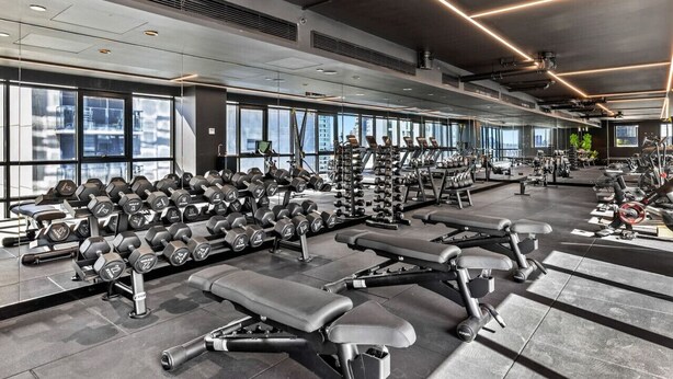 Une salle de sport moderne dotée de divers appareils d’exercice, de grandes fenêtres et d’un plafond haut.