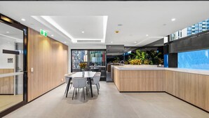 Un hall d’hôtel moderne comprenant un comptoir d’accueil, un espace salon avec une table et des chaises, et une grande fenêtre donnant sur la ville.