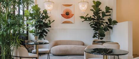 Un salon moderne avec un canapé, deux tables rondes et de grandes plantes.