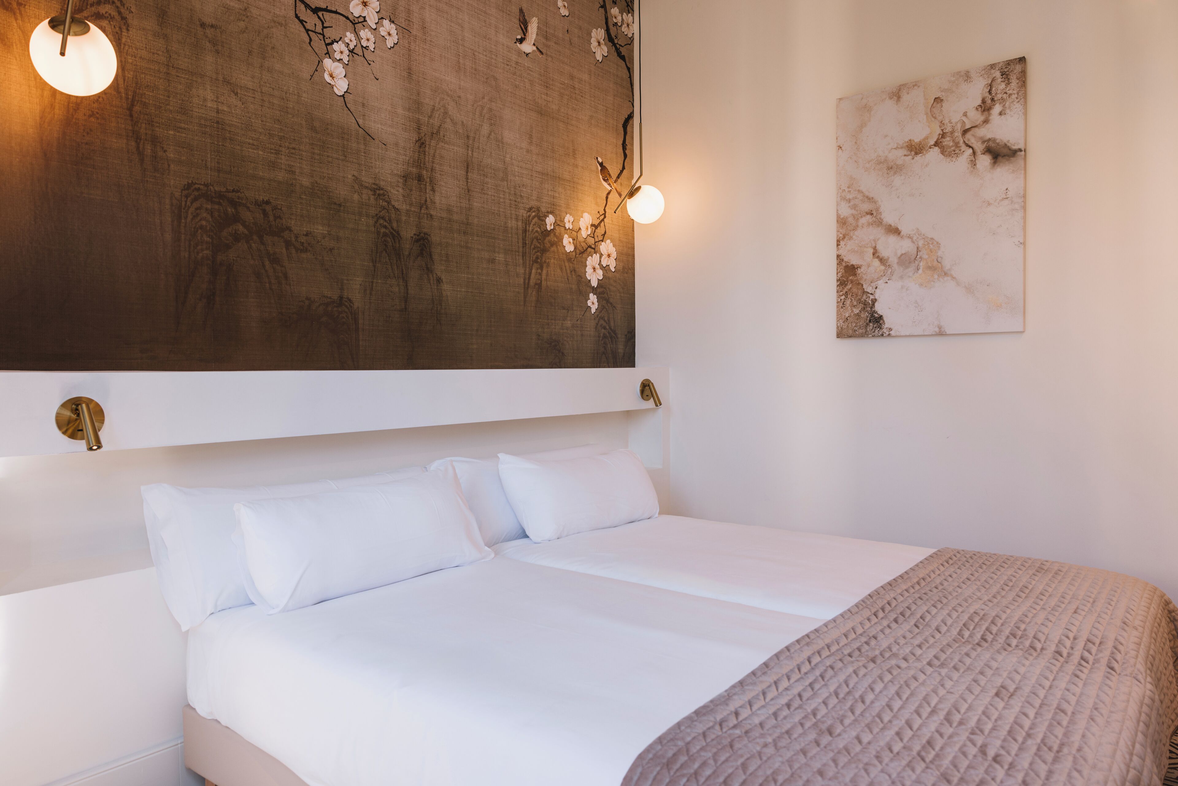 A bed with white linens, a wooden headboard with wall art, and a single hanging light fixture.