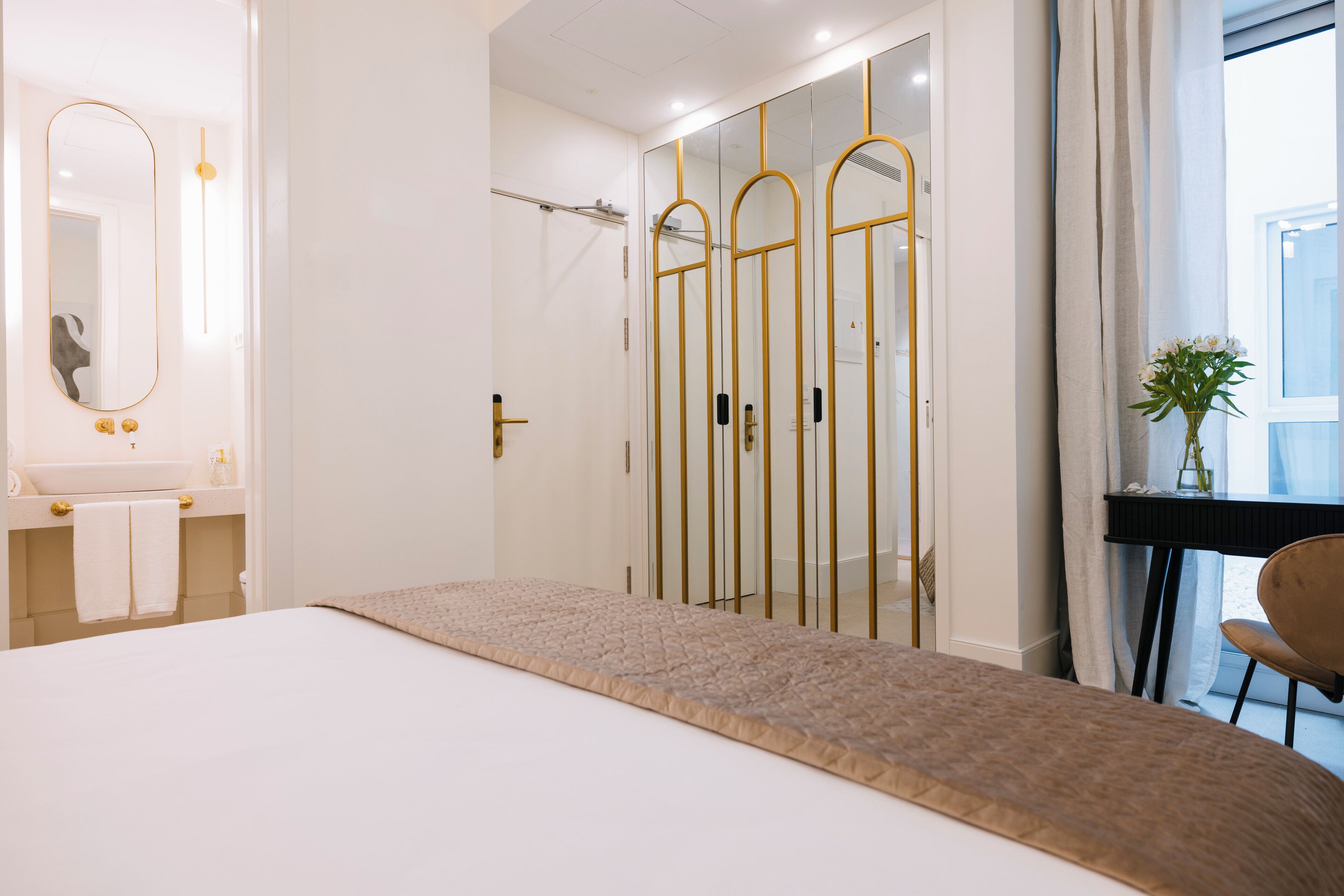 A modern hotel room with a large bed, a vanity with a mirror, and a walk-in closet with a mirror.