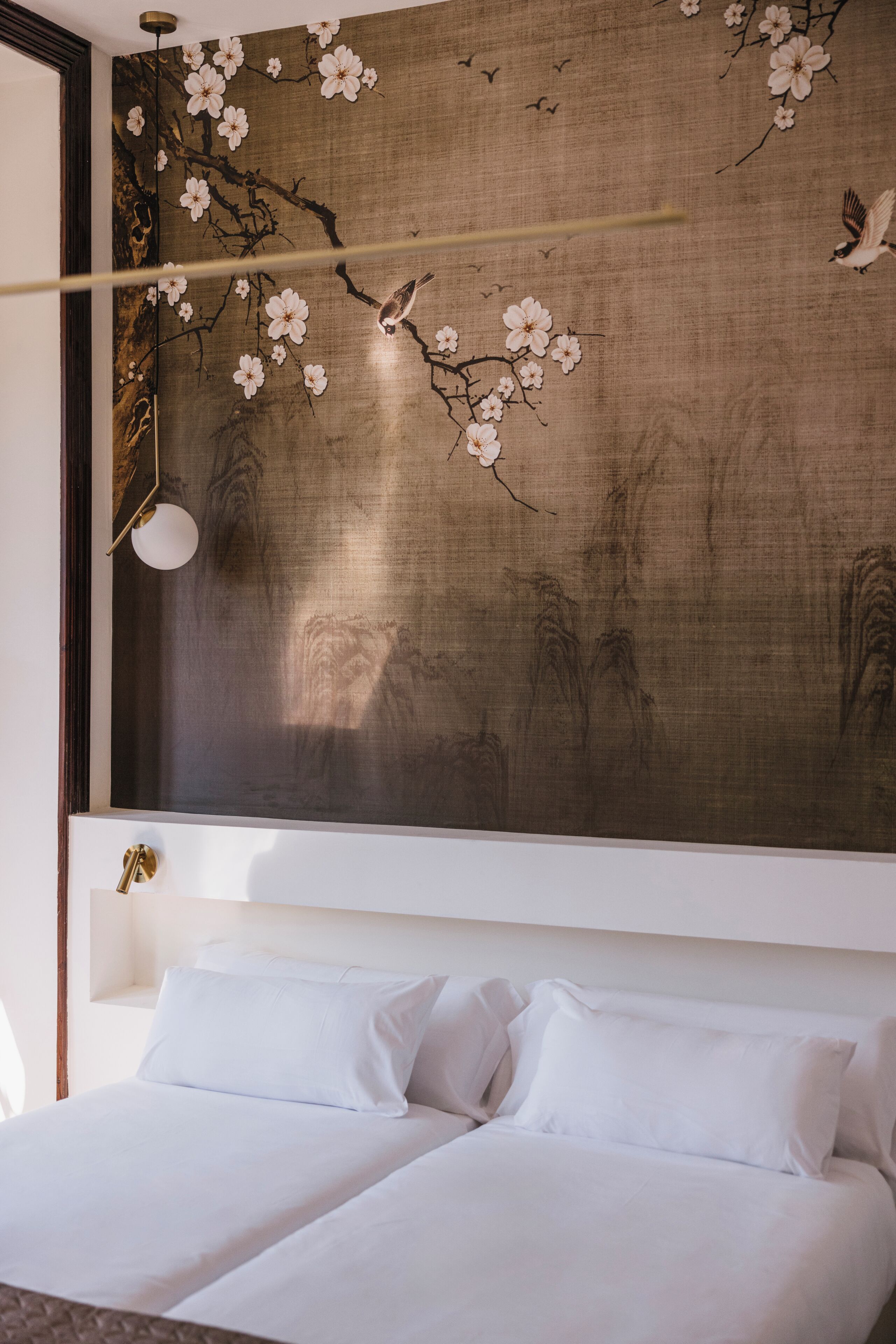Ein Schlafzimmer mit einem großen Bett, einer Wandleuchte und einer Wand mit floralen und Vogelmotiven.