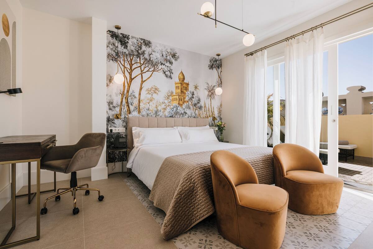 Une chambre à coucher avec un lit, deux chaises, un bureau et une fresque murale.