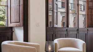 A room with two armchairs, a small table with a lamp, and large windows with a view of buildings. -  MASANET Emblematic Hotels by Airnest (Las Palmas de Gran Canaria)