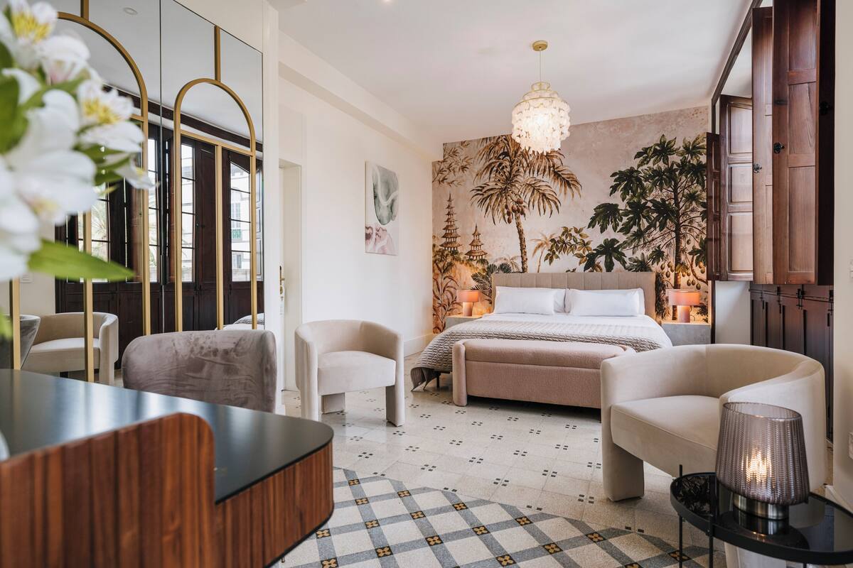 Une chambre moderne avec un lit, deux chaises, un bureau et un grand miroir.