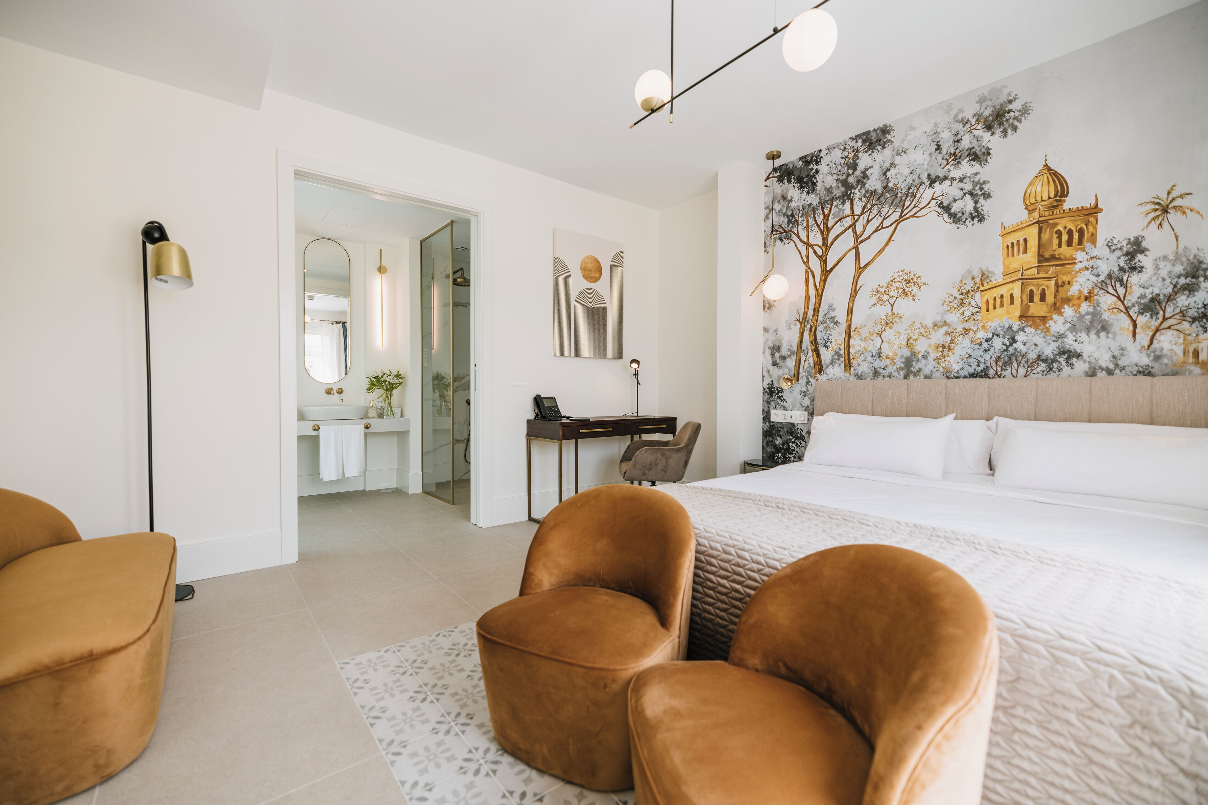 Ein Schlafzimmer mit einem großen Bett, zwei braunen Sesseln, einem Schreibtisch und einem Wandbild eines Gebäudes.