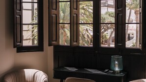 A room with a checkered floor, a desk, two chairs, and a window with a view of palm trees. -  MASANET Emblematic Hotels by Airnest (Las Palmas de Gran Canaria)