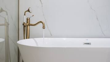 A modern bathroom with a freestanding bathtub, a glass shower enclosure, and a marble wall.
