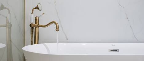 Un baño moderno con una bañera independiente, cabina de ducha con mampara de vidrio y pared de mármol.