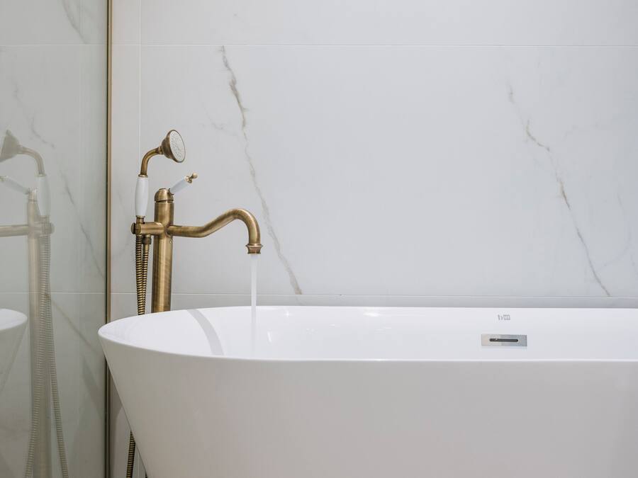 A modern bathroom with a freestanding bathtub, a glass shower enclosure, and a marble wall.