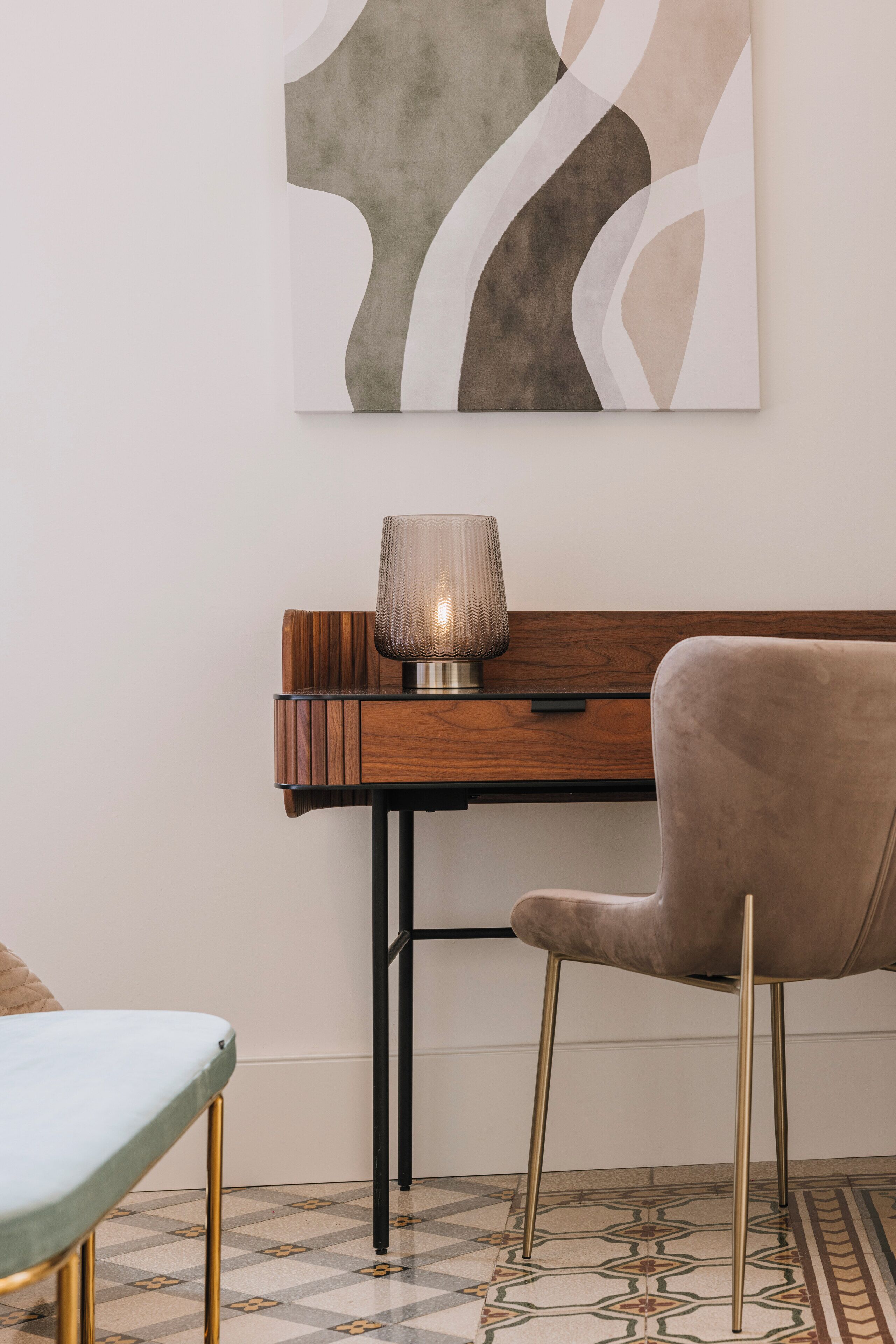 A modern room with a wooden desk, a lamp, a plush chair, and a geometric patterned rug.