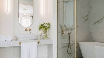 A modern bathroom with a white sink, a large mirror, a glass-enclosed shower, and a freestanding bathtub.