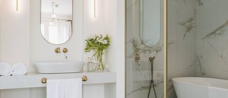 Un baño moderno con lavamanos blanco, un espejo grande, ducha con mampara de vidrio y bañera independiente.
