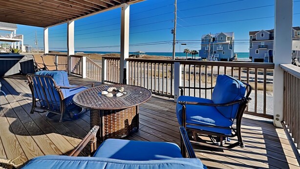 A covered outdoor deck with blue cushioned chairs, a round table with decorative stones, and a view of the beach and ocean. - Family Tides | Spacious Oceanfront Home, Sound Views + Hot Tub! (North Topsail Beach)