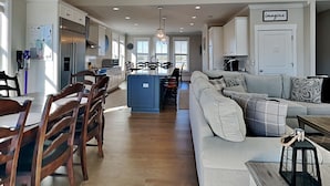 A spacious kitchen with a central island, wooden dining chairs, a sofa, and a coffee table. - Family Tides | Spacious Oceanfront Home, Sound Views + Hot Tub! (North Topsail Beach)