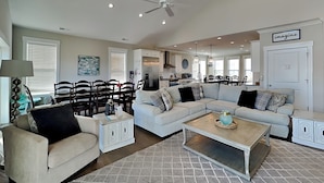 A spacious living room with a large sectional sofa, a coffee table, and a dining area with chairs and a table. - Family Tides | Spacious Oceanfront Home, Sound Views + Hot Tub! (North Topsail Beach)