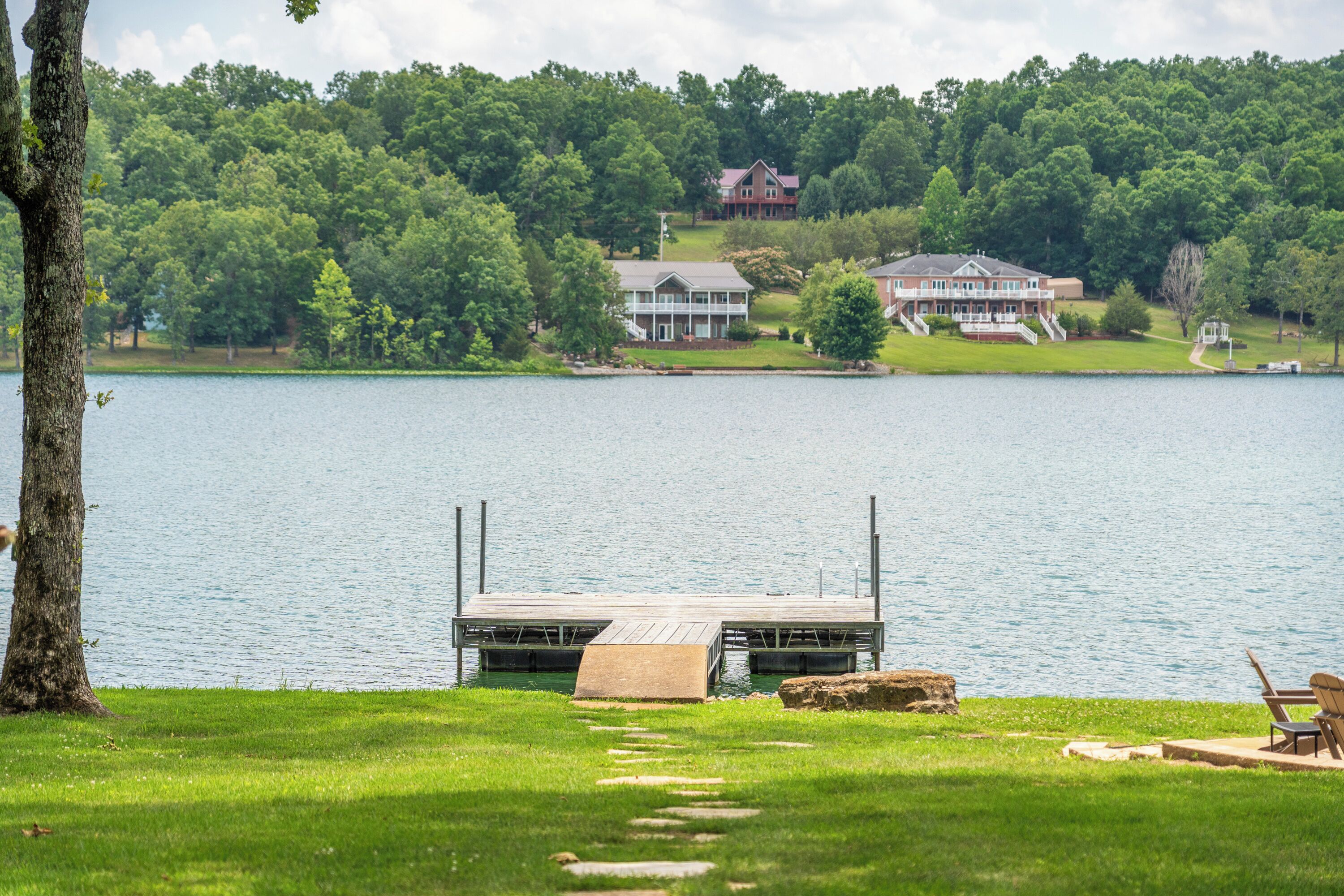 A lakeside property with a dock, a grassy area, and a large house in the background.