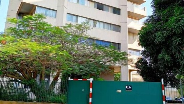 Een hoog woongebouw met meerdere balkons, een hekpoort en omliggend groen.