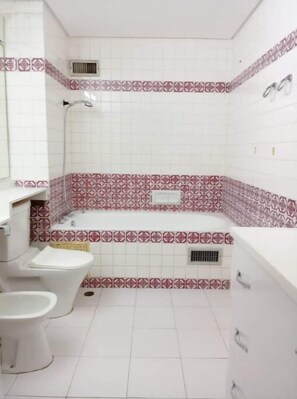 A bathroom with a toilet, bidet, and bathtub, featuring patterned tiles and white fixtures. - Avenue Lamblin Abidjan (Abidjan)