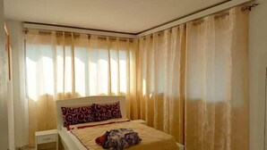 Een slaapkamer met een bed, gordijnen en een nachtkastje.