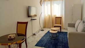 Een woonkamer met een televisie, een eettafel, een blauw vloerkleed en een bank.